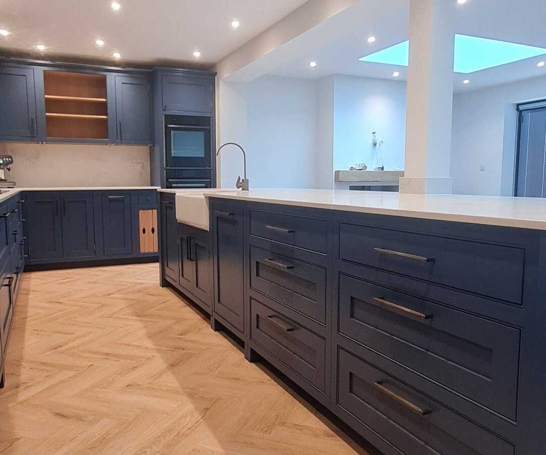 A navy shaker kitchen with a Belfast sink in the island and a herringbone floor