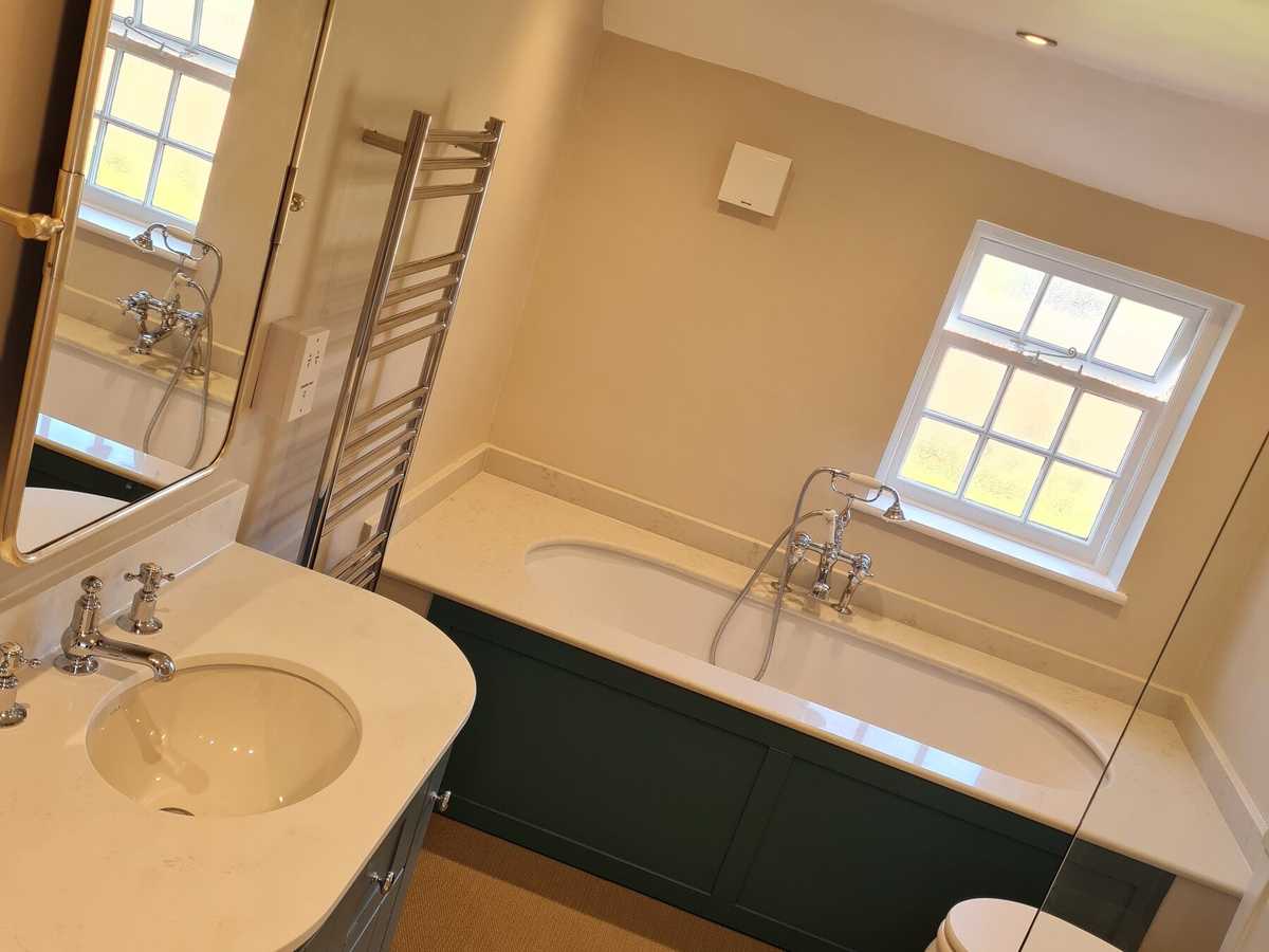 A bath with a painted panel beneath a sash window, and a curved vanity unit