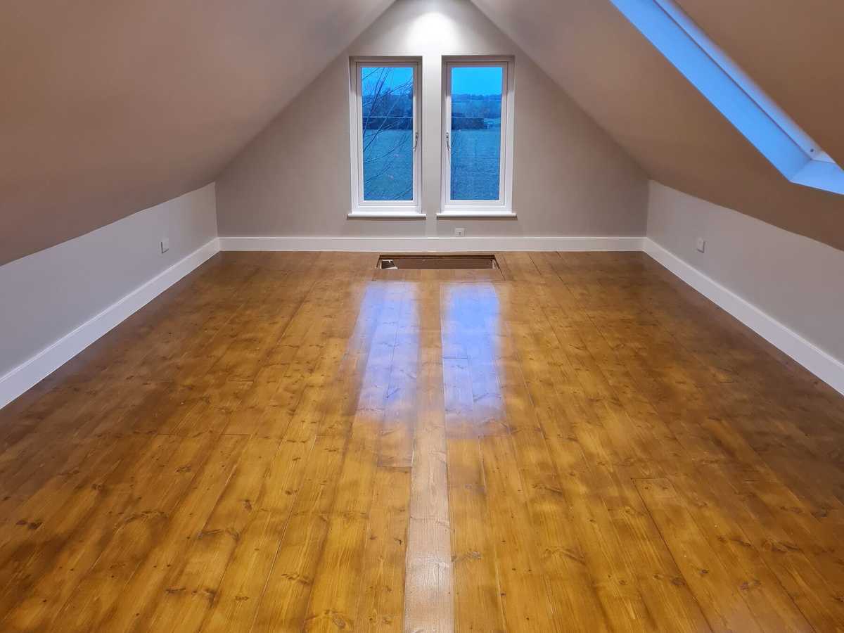 A loft room with a sanded wooden floor and a roof window