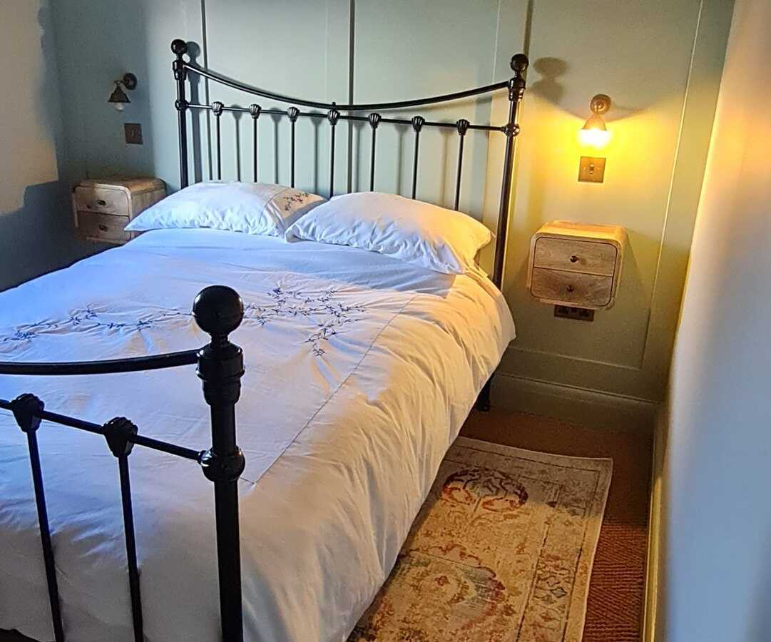 A bedroom with panelled walls, an iron bed and wall lights