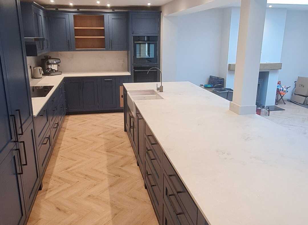 A navy shaker kitchen with a long white-topped island and a herringbone floor