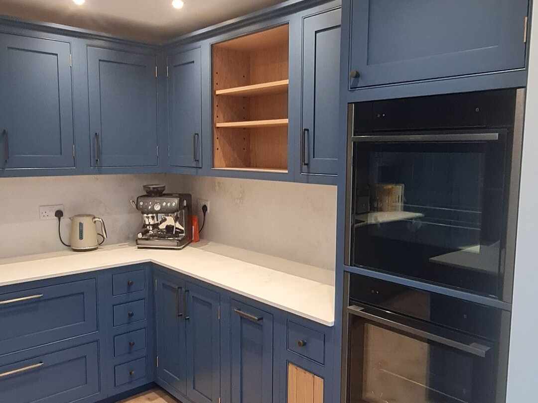 Built-in ovens beside navy units with oak-lined open shelves